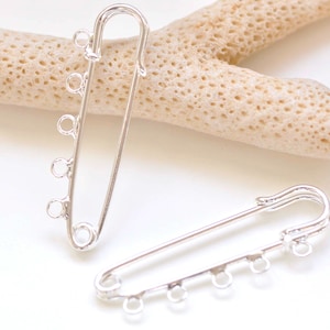 Puede incluir: Dos imperdibles plateados con múltiples anillas de salto. Los imperdibles están sobre una superficie blanca.