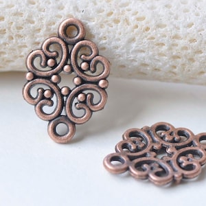 Pode incluir: Dois encantos de filigrana de cobre antigo com forma quadrada e um design intrincado de volutas. Os encantos têm um furo na parte superior para serem presos a joias ou outras manualidades.