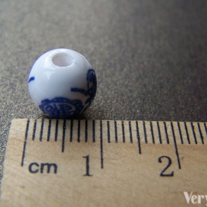 Puede incluir: Una cuenta de cer&aacute;mica blanca con un dise&ntilde;o floral azul. La cuenta mide aproximadamente 1 cm de di&aacute;metro.