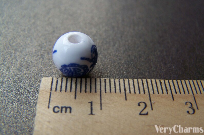 Puede incluir: Una cuenta de cer&aacute;mica blanca con un dise&ntilde;o floral azul. La cuenta mide aproximadamente 1 cm de di&aacute;metro.