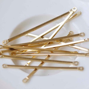 May include: A group of gold-colored metal jump rings with a loop on each end. The rings are arranged in a pile on a white surface.
