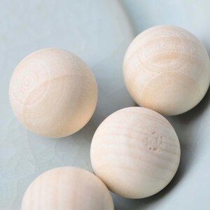 Puede incluir: Cuatro bolas de madera lisas en un cuenco azul claro. Las bolas son de color beige claro y tienen una veta de madera natural.