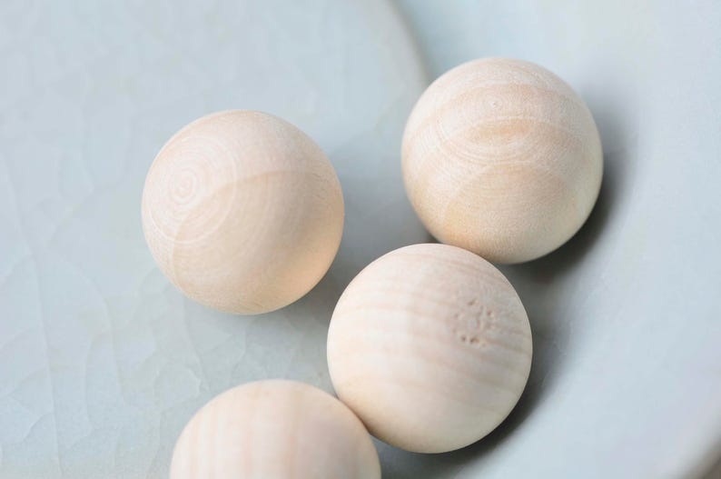 Puede incluir: Cuatro bolas de madera lisas en un cuenco azul claro. Las bolas son de color beige claro y tienen una veta de madera natural.