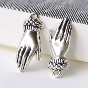 May include: Two silver-toned metal charms shaped like hands with a detailed design. The charms have a loop at the top for attaching to jewellery or other crafts.