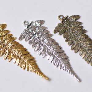 Könnte beinhalten: Drei metallene Glücksbringer in Form von Farnen in Gold, Silber und Bronze.