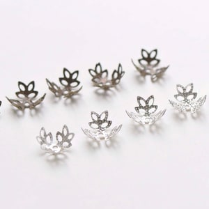 May include: A collection of silver and gold metal bead caps with a flower design. The caps are open and ready to be used for jewelry making.
