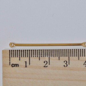 May include: A gold-colored metal bar with two small loops at each end. The bar is approximately 3 cm long.