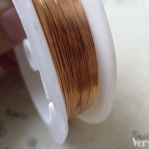 May include: A spool of copper wire wound around a white plastic bobbin. The wire is thin and has a shiny, metallic finish.