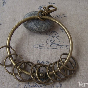 May include: A bronze key ring with a large circular ring and several smaller rings attached. The key ring is on a beige fabric background.