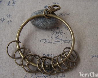 Könnte beinhalten: Ein Schlüsselring aus Bronze mit einem großen runden Ring und mehreren kleineren Ringen, die daran befestigt sind. Der Schlüsselring liegt auf einem beigefarbenen Stoffhintergrund.