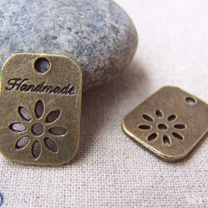 May include: Two antique gold-toned metal tags with a flower design and a hole for string. One tag says "Handmade".