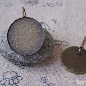 May include: Two bronze-colored earring blanks with a round shape and a hook closure. The blanks are ready to be customized with your own designs.