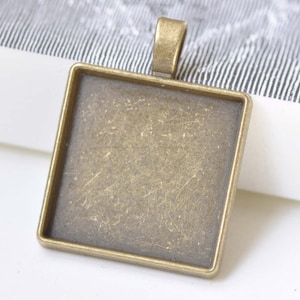 May include: Square pendant tray with a bronze finish. The pendant has a loop at the top for attaching to a chain. The tray is empty, ready for customization. Ideal for jewelry making and crafting.