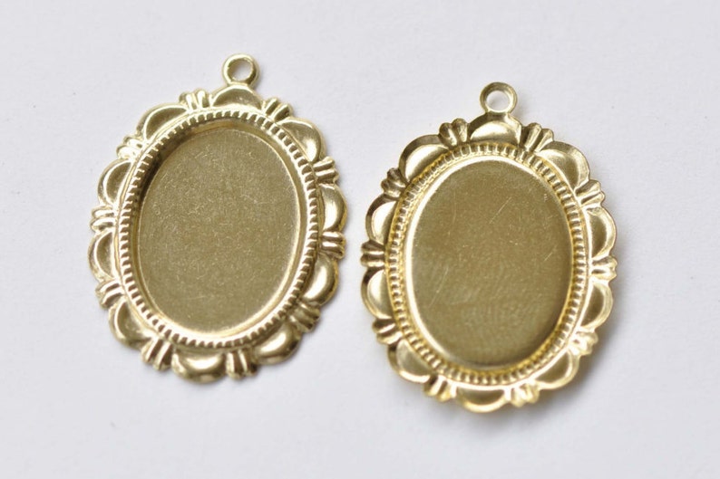 Peut inclure: Deux plateaux de pendentif ovales en m&eacute;tal de couleur dor&eacute;e avec un bord festonn&eacute; d&eacute;coratif. Les plateaux sont vierges et pr&ecirc;ts &agrave; &ecirc;tre remplis de r&eacute;sine, de photos ou d'autres embellissements.