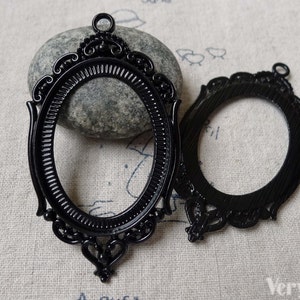 Op de afbeelding: Twee ovale fotolijsten van zwart metaal met sierlijke details. De lijsten hebben een gestructureerde afwerking en een lus aan de bovenkant om op te hangen.