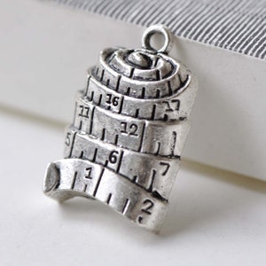 Può includere: Ciondolo in metallo color argento a forma di metro a nastro arrotolato con i numeri 1, 5, 6, 7, 22, 27, 32 e 36 visibili.