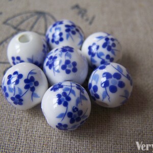 Puede incluir: Un grupo de siete cuentas de cer&aacute;mica blanca con un dise&ntilde;o floral azul. Las cuentas son redondas y tienen un acabado brillante.