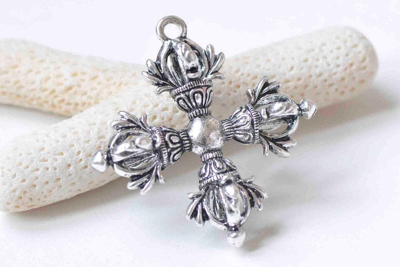 May include: Silver-toned metal pendant in the shape of a cross with intricate details. Each arm of the cross features a decorative design with a crown-like top.