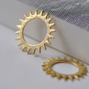 Puede incluir: Dos anillos de color dorado en forma de sol con una superficie texturizada. Los anillos son de metal y tienen una forma circular con un borde puntiagudo.