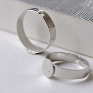 May include: Two silver ring blanks, one with a round bezel, for jewelry making.
