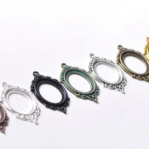 May include: Seven oval-shaped metal frames with ornate detailing in various colors, including copper, silver, black, green, and gold. The frames are designed for jewelry making or crafting.