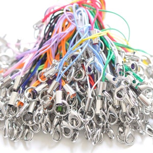 May include: A large pile of colorful string phone charms with silver metal clasps. The charms are made of thin, colorful cords with a silver metal bead at the end.