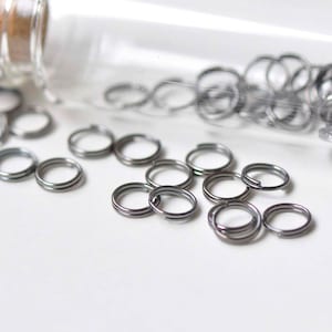 May include: A glass jar filled with silver jump rings. The jar is laying on its side and some of the jump rings have spilled out.