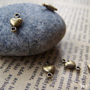 May include: A close-up of antique gold heart-shaped jump rings. The rings are on a gray stone and a piece of paper with text.