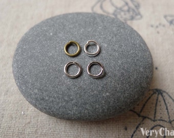 May include: Four jump rings, two silver and two bronze, on a gray stone surface.