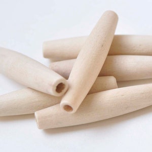 May include: A group of six unfinished wooden dowels, all of the same size and shape, are arranged in a pile on a white surface. The dowels are smooth and have a natural wood colour.