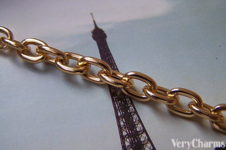 May include: Gold chain link with oval shaped links. The chain is lying on a surface with a blurred image of the Eiffel Tower in the background.