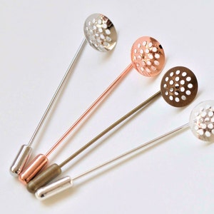 May include: Four decorative pins with different colored metal tops. The tops are round and have a honeycomb pattern. The pins are silver, copper, bronze, and gold.