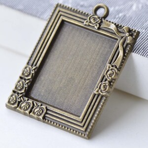 May include: A bronze-colored metal picture frame pendant with a decorative rose and ribbon design. The frame has a blank space for inserting a photo or other small object.