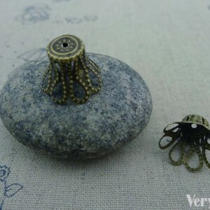 May include: Two antique gold metal decorative end caps for jewelry making. The end caps have a scalloped design with a small hole in the center.