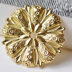May include: A gold-toned metal decorative accent with a circular shape and intricate floral designs. The center of the accent has a small hole.