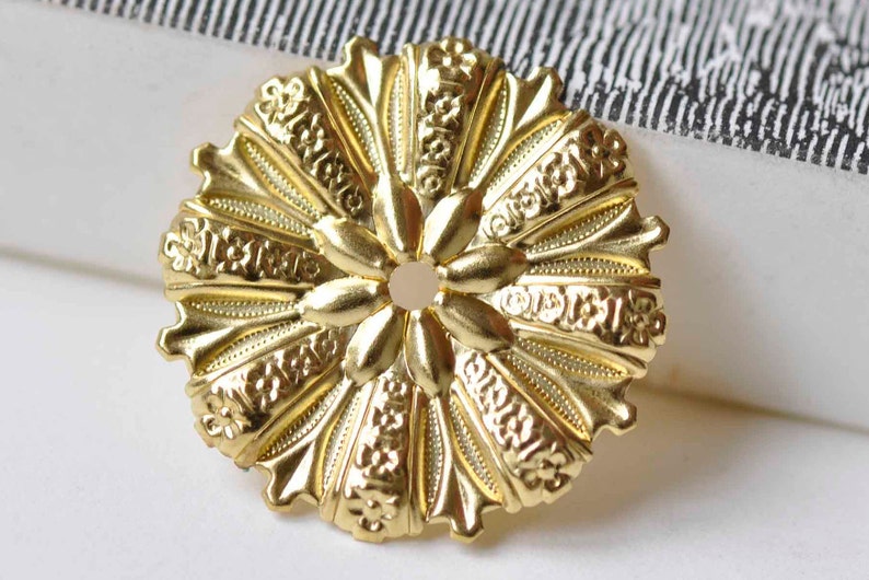 May include: A gold-toned metal decorative accent with a circular shape and intricate floral designs. The center of the accent has a small hole.