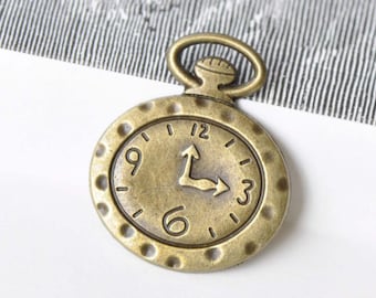 May include: A bronze-colored pocket watch charm with a round face and a loop at the top. The face has Roman numerals for the hours and a stylized hand pointing to the 3.