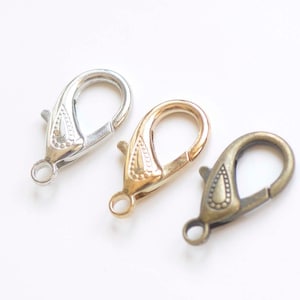 May include: Three metal lobster clasps in silver, gold, and bronze finishes. Each clasp has a decorative design.