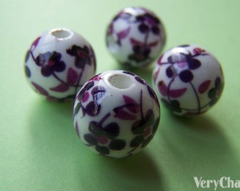 Può includere: Quattro perline in ceramica bianca con un motivo floreale viola e rosa. Le perline sono rotonde e hanno un foro al centro.