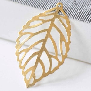 May include: A gold leaf charm with a delicate, intricate design. The leaf is cut out, creating a lacy effect. It is a perfect embellishment for jewelry making or crafting projects.