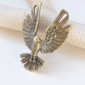 May include: A gold-toned metal dove charm with detailed wings and a delicate design. The dove is in flight with its wings spread wide.