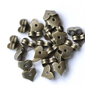 Op de afbeelding: Een stapel antieke gouden hartvormige metalen bedels met een klein gaatje in het midden van elk hart. De bedels hebben een decoratief ontwerp en de tekst "24" is op elke bedel gegraveerd.