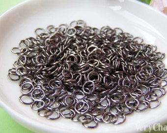 May include: A white ceramic dish filled with a large quantity of small, silver-toned jump rings. The rings are all the same size and are arranged in a random pattern.