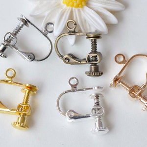 Op de afbeelding: Vijf schroefbevestigde oorclips in verschillende afwerkingen: zilver, goud en brons. De clips zijn ontworpen om op de oorlel te worden gedragen en hebben een schroefbevestiging om ze op hun plaats te houden.