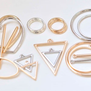 May include: Assortment of metal jewellery findings in gold, silver, and rose gold finishes.  The findings include a heart, oval, circle, and triangle shapes.  Some of the findings have a bar or loop for attaching to jewellery.