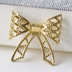 Könnte beinhalten: Eine goldene Schleife aus Metall mit geometrischem Muster. Die Schleife ist aus dünnem Metall gefertigt und hat ein zartes, filigranes Muster.