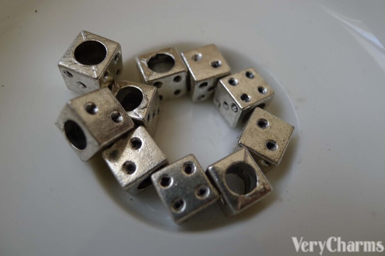 May include: A group of silver metal dice charms with holes in the center. The dice are arranged in a circle on a white surface.