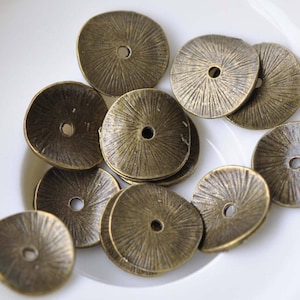 May include: A group of 10 antique gold-toned metal round beads with a raised design. The beads have a hole in the centre for stringing.