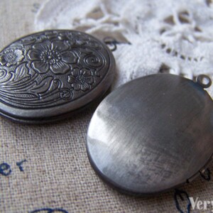 May include: Two silver oval locket pendants. One pendant has a floral design and the other is plain. Both pendants have a loop for attaching a chain.