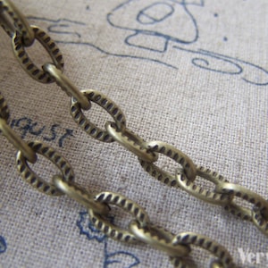 May include: A close-up of a gold-toned chain with oval links. The chain has a textured, ribbed design.